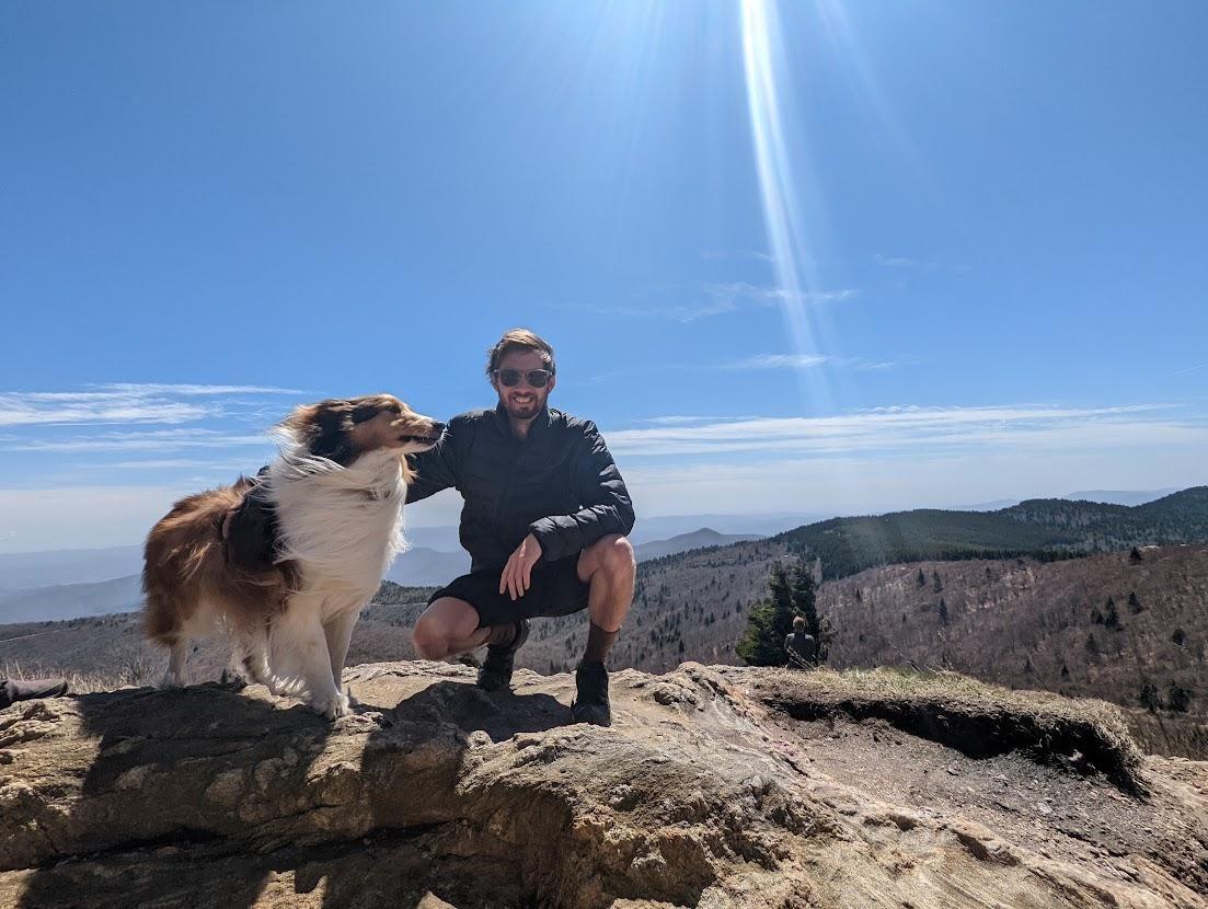 Person petting a dog on top of the mountains